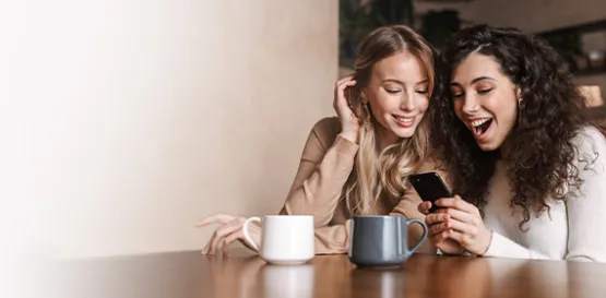 two girls sitting by the table looking at the mobile phone and laughing